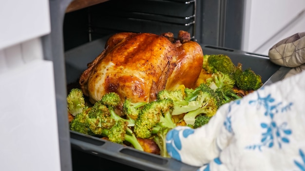 Señora saca pollo crujiente con verduras en una bandeja para hornear del horno.