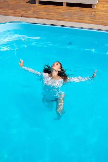 Señora sensual en vestido mojado de pie en la piscina durante las vacaciones de verano