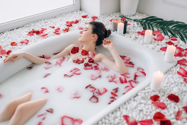 Señora sexy en el baño con espuma y pétalos de rosa