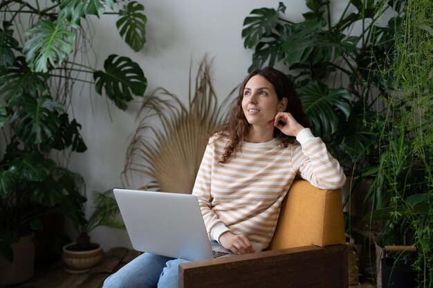 Señora soñadora pensativa mirando hacia otro lado esperando inspiración plantas verdes exóticas en el fondo