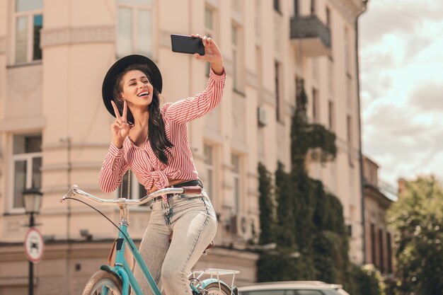 Señora sonriente en la bicicleta que muestra un gesto de paz para un selfie. Banner de plantilla