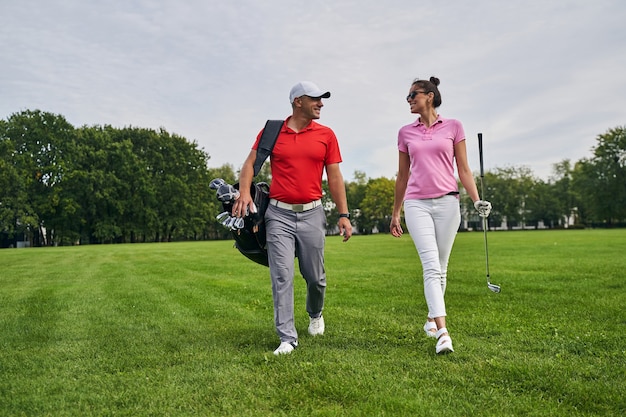 Señora sonriente con un palo de golf caminando junto a un entrenador profesional