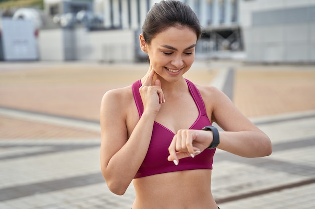 Señora sonriente en la parte superior de los deportes mirando smartwatch