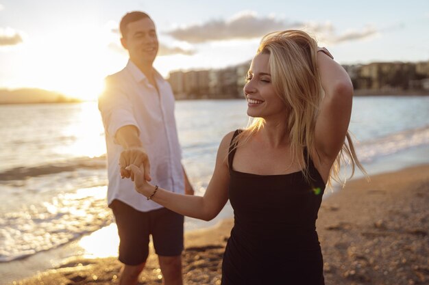 Señora sonriente con vestido negro de pie junto al mar con el hombre