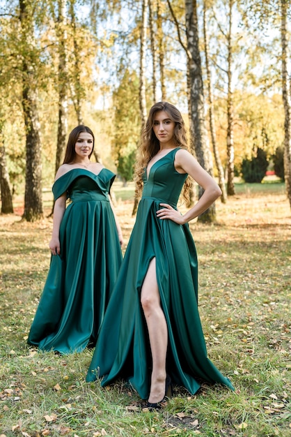 Señoras en elegantes vestidos verdes caminando en el parque de otoño. Chica morena Chicas jóvenes de ensueño riendo al aire libre