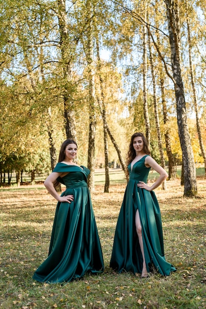 Señoras en elegantes vestidos verdes caminando en el parque de otoño. Chica morena Chicas jóvenes de ensueño riendo al aire libre