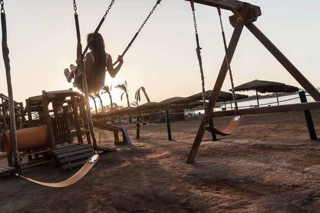 Foto señorita cabalgando sobre un columpio al atardecer sobre un fondo de palma t