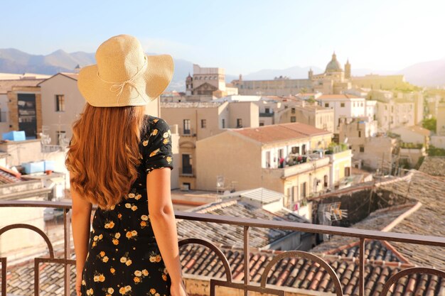 Señorita mirando el paisaje urbano de Palermo desde el balcón al atardecer en Italia