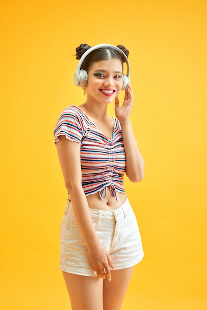 Señorita con moños y escuchando música con auriculares sobre fondo amarillo