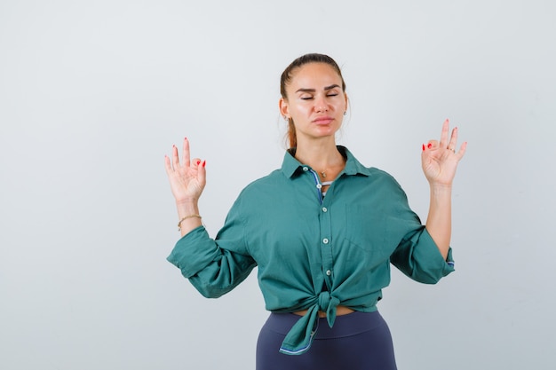 Señorita mostrando gesto de yoga con los ojos cerrados en camisa verde y mirando relajado. vista frontal.