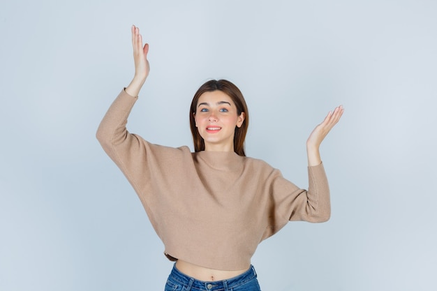 Señorita mostrando signo de tamaño en suéter beige, jeans y mirando alegre. vista frontal.