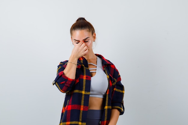 Señorita en la parte superior, camisa a cuadros frotándose la nariz y los ojos y con aspecto cansado, vista frontal.