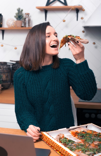 Foto la señorita que acaba de recibir su pizza ordenada está comiendo una porción.