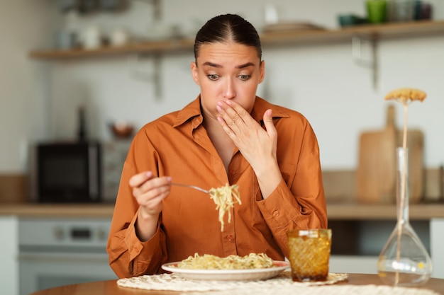 Foto señorita que siente náuseas mientras come espagueti entregado mujer mirando el plato y cerrando la boca