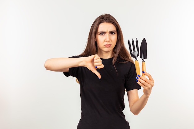 Señorita sosteniendo herramientas de jardinería y gesto pulgar hacia abajo