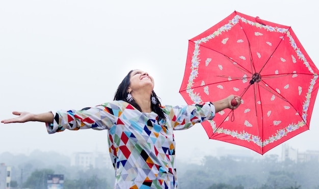 Una señorita sosteniendo paraguas y abrazando la lluvia con las manos estiradas hacia el cielo durante el monzón