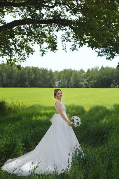 Señorita en un vestido de novia posando en la pradera en el día de verano