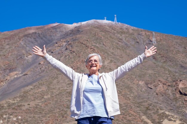 Sensación de libertad para una anciana sonriente de cabello blanco de pie con los brazos abiertos en el fondo de la montaña Anciana feliz disfrutando de viajes y vacaciones