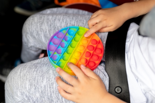 Sensorial anti-stress brinquedos pop nas mãos de uma criança. um menino criança feliz brinca com um brinquedo de covinha simples no carro.