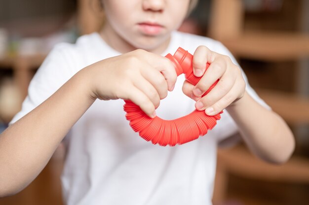 Sensorisches Anti-Stress-Kunststoffspielzeug in Kinderhänden. ein kleiner glücklicher kinderjunge spielt zu hause mit einem poptube-zappelspielzeug. Kinder halten und spielen Pop Tube rote Farbe, Trend 2021 Jahr