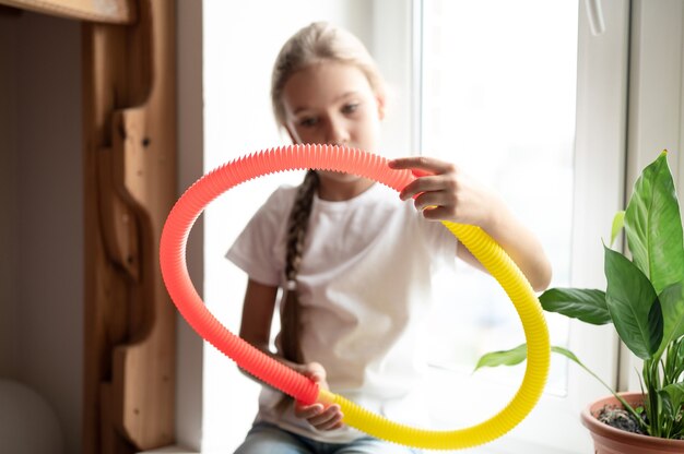 Sensorisches Anti-Stress-Kunststoffspielzeug in Kinderhänden. ein kleines glückliches kindermädchen spielt zu hause mit einem poptube-zappelspielzeug. Kinder, die Pop-Röhre in gelber und roter Farbe halten und spielen, Trend 2021-Jahr