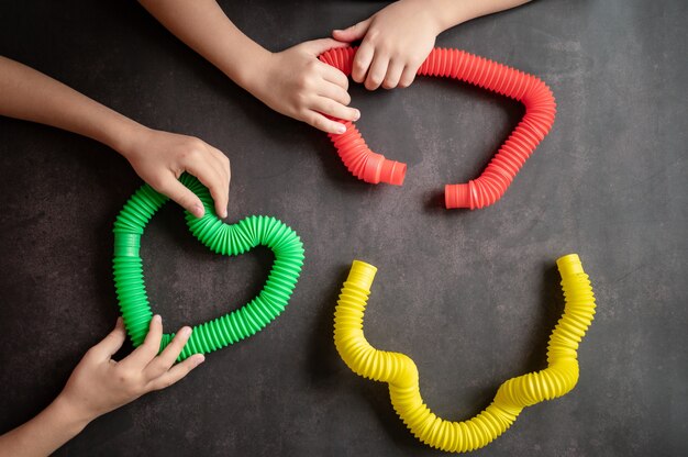 Sensorisches Anti-Stress-Pop-Tube-Spielzeug in Kinderhänden. Ein kleines glückliches Kind spielt mit einem Poptube-Spielzeug auf einem schwarzen Tisch. Kleinkinder, die Pop-Röhren halten und spielen, mehrfarbige helle Farbe, Trend 2021-Jahr
