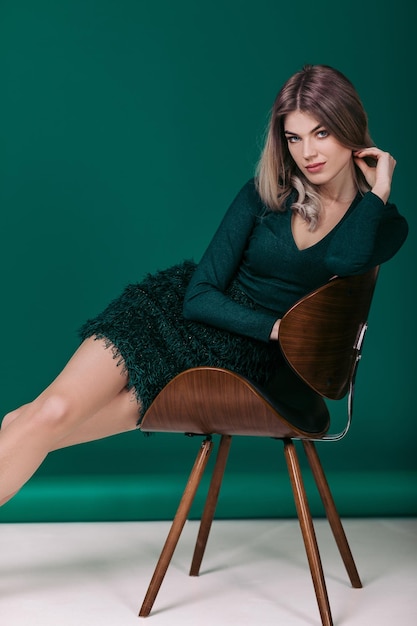 Sensual hermosa mujer rubia en vestido verde sentada en una silla contra un fondo verde