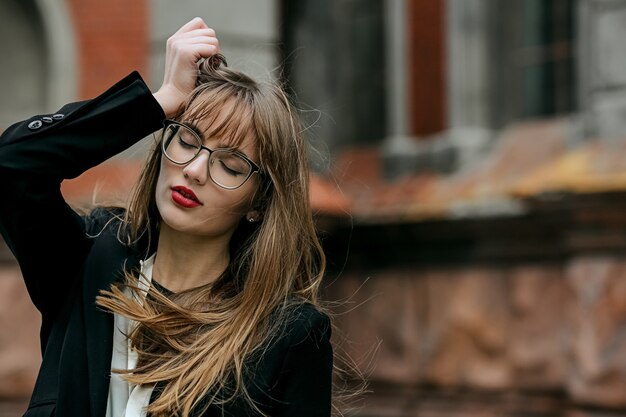 Sensual mujer joven con lápiz labial rojo viste traje y gafas posando en el antiguo edificio en Kiev. Espacio para texto