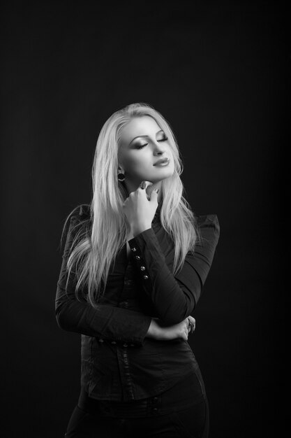 Sensual mujer rubia con maquillaje perfecto y pelo largo y recto lleva blusa, posando en el estudio. Disparo en blanco y negro