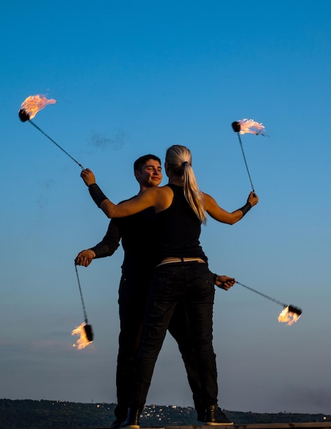 Sensual pareja de artistas de fuego bailan con poi en llamas en el cielo azul al aire libre deseo