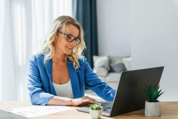 Senta-se à mesa com laptop Mulher em roupas casuais está dentro de casa em casa