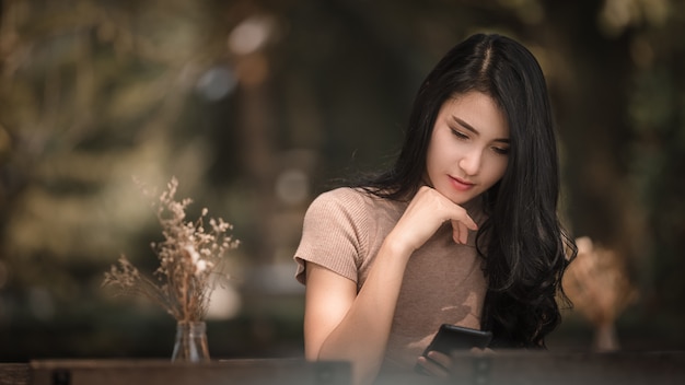 La sentada asiática hermosa de la muchacha de las mujeres está comprobando masaje en el teléfono móvil en el parque