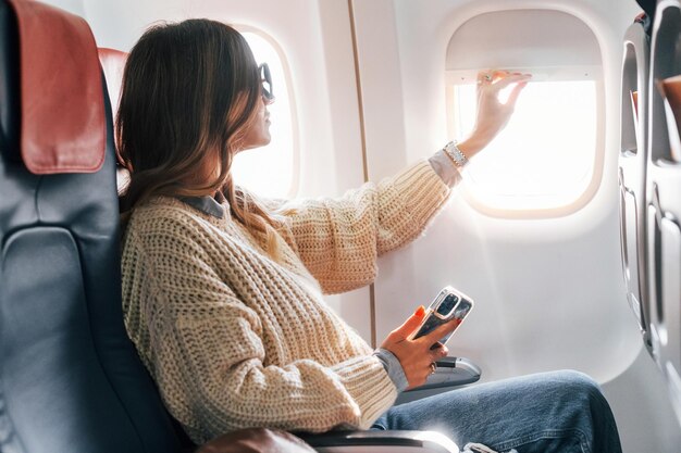 Foto sentada com o telemóvel nas mãos, uma jovem passageira de roupa casual está no avião.