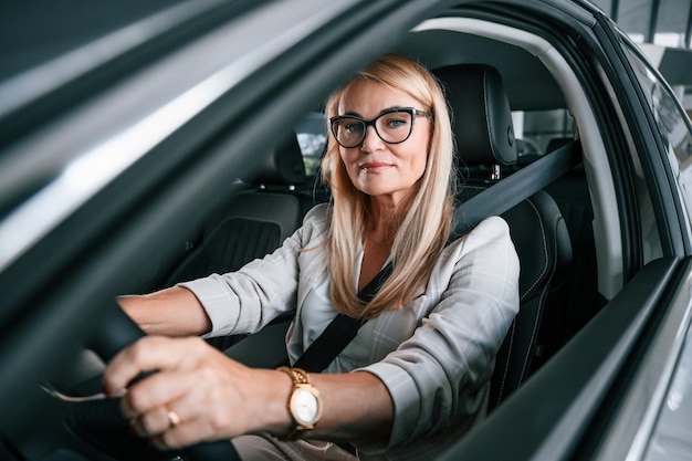 Foto sentada dentro do novo automóvel mulher com roupas formais brancas está na concessionária