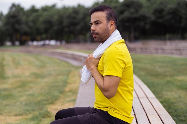 Sentado en un banco de madera en el parque verde de la ciudad, un hombre guapo descansa durante su entrenamiento de rutina.