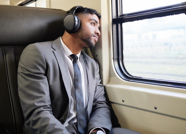 Sentado com seus pensamentos um pouco. Foto de um jovem empresário usando fones de ouvido enquanto olhava pela janela em um trem durante seu trajeto.