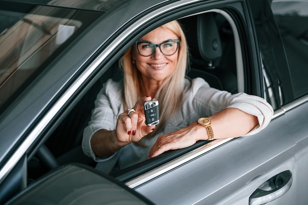 Sentado dentro del nuevo automóvil Mujer en ropa formal blanca está en el concesionario de automóviles