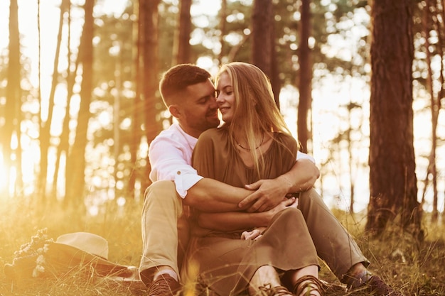 Sentado e abraçando um ao outro casal feliz está ao ar livre na floresta durante o dia