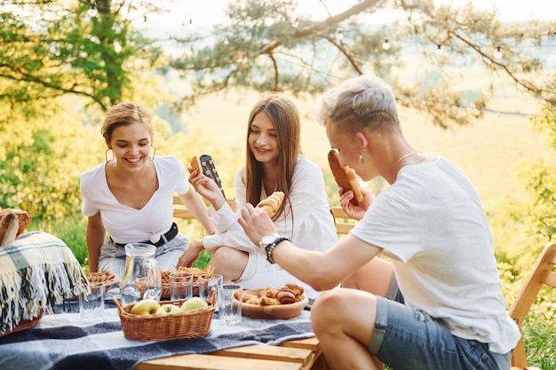 Sentado junto a una mesa de picnic Grupo de jóvenes tienen vacaciones al aire libre en el bosque Concepción de fin de semana y amistad