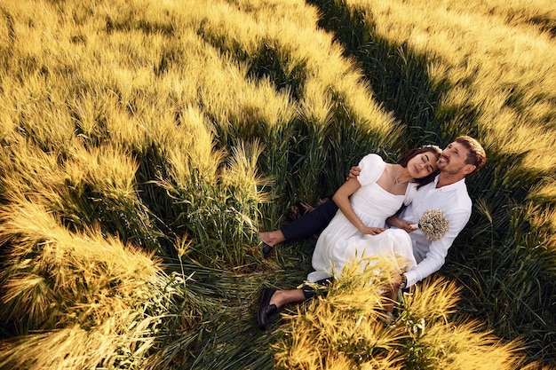 Sentado no chão Casal recém-casado Juntos no majestoso campo agrícola em dia ensolarado