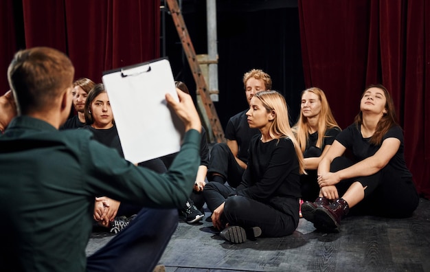 Sentado no chão Grupo de atores em roupas de cor escura em ensaio no teatro