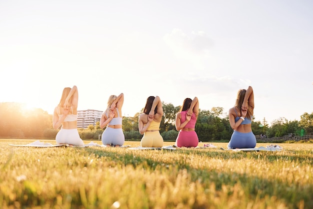 Sentado en posición de loto Grupo de mujeres tienen fitness al aire libre en el campo juntos