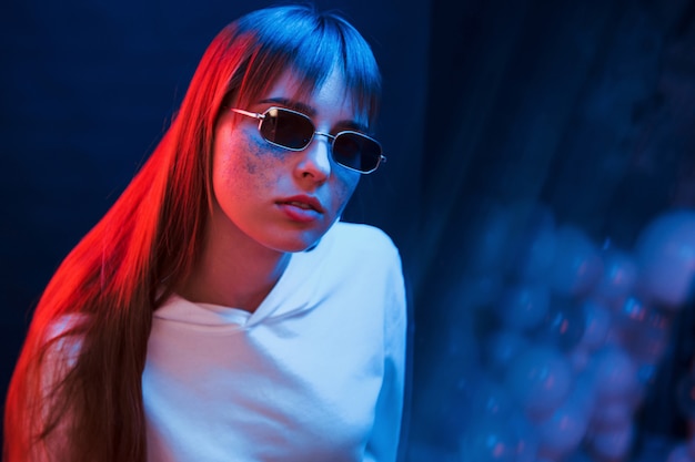 Sentado y relajado. Foto de estudio en estudio oscuro con luz de neón. Retrato, de, niña joven