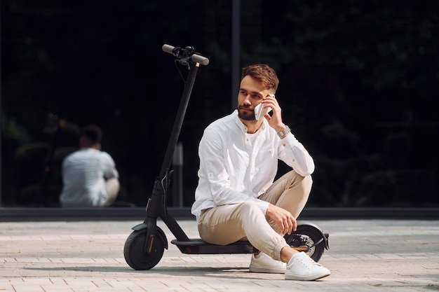 Sentado en el scooter El hombre elegante está al aire libre durante el día