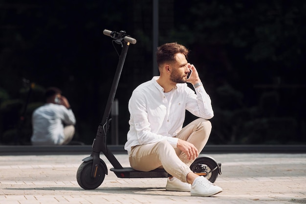 Sentado en el scooter El hombre elegante está al aire libre durante el día