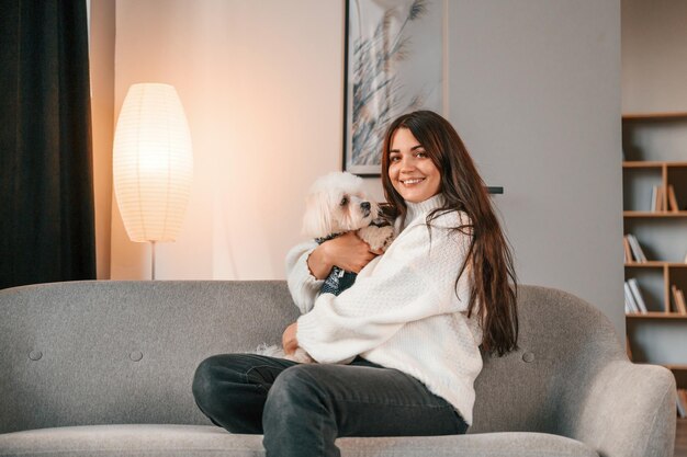 Foto sentado en el sofá hermosa mujer está con perro maltés está en casa