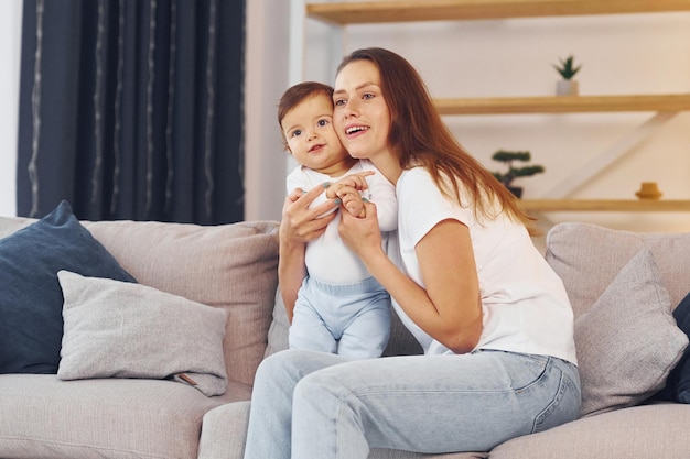 Sentado en el sofá Madre con su pequeña hija está en casa juntos