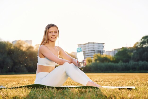 Sentado en el suelo posando y descansando Hermosa mujer en ropa deportiva haciendo ejercicios de fitness al aire libre en el campo