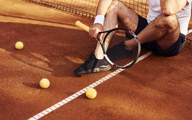 Sentado y tomando un descanso Vista de cerca del hombre mayor con camisa blanca y pantalones cortos deportivos negros que está en la cancha de tenis