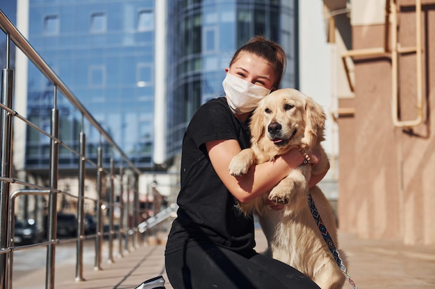 Sentados juntos Joven mujer positiva con máscara protectora da un paseo al aire libre cerca del edificio comercial en tiempo de cuarentena Concepción del coronavirus